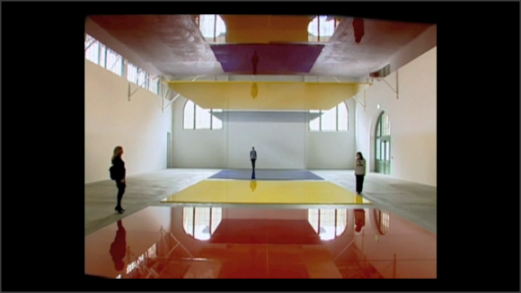 Foto de una instalación. Personas caminan por una enorme sala con enormes placas de color en suelo y techo