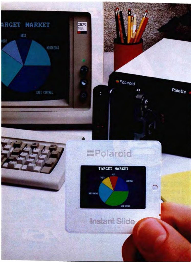 Foto. En el fondo hay un ordenador IBM PC con un diagrama de sectores. A su lado, un dispositivo de la marca Polaroid, con el nombre de modelo Palette, al que alguien ha juntado una cámara réflex. En primer plano, una mano sostiene una diapositiva con el mismo diagrama de sectores, en colores mucho más vibrantes que los de la pantalla